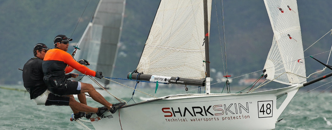 Sailing vessel with 2 men leaning over to balance the craft wearing Sharkskin Performance wear